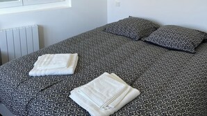 A bedroom with a bed, pillows, a window, and a painting on the wall.