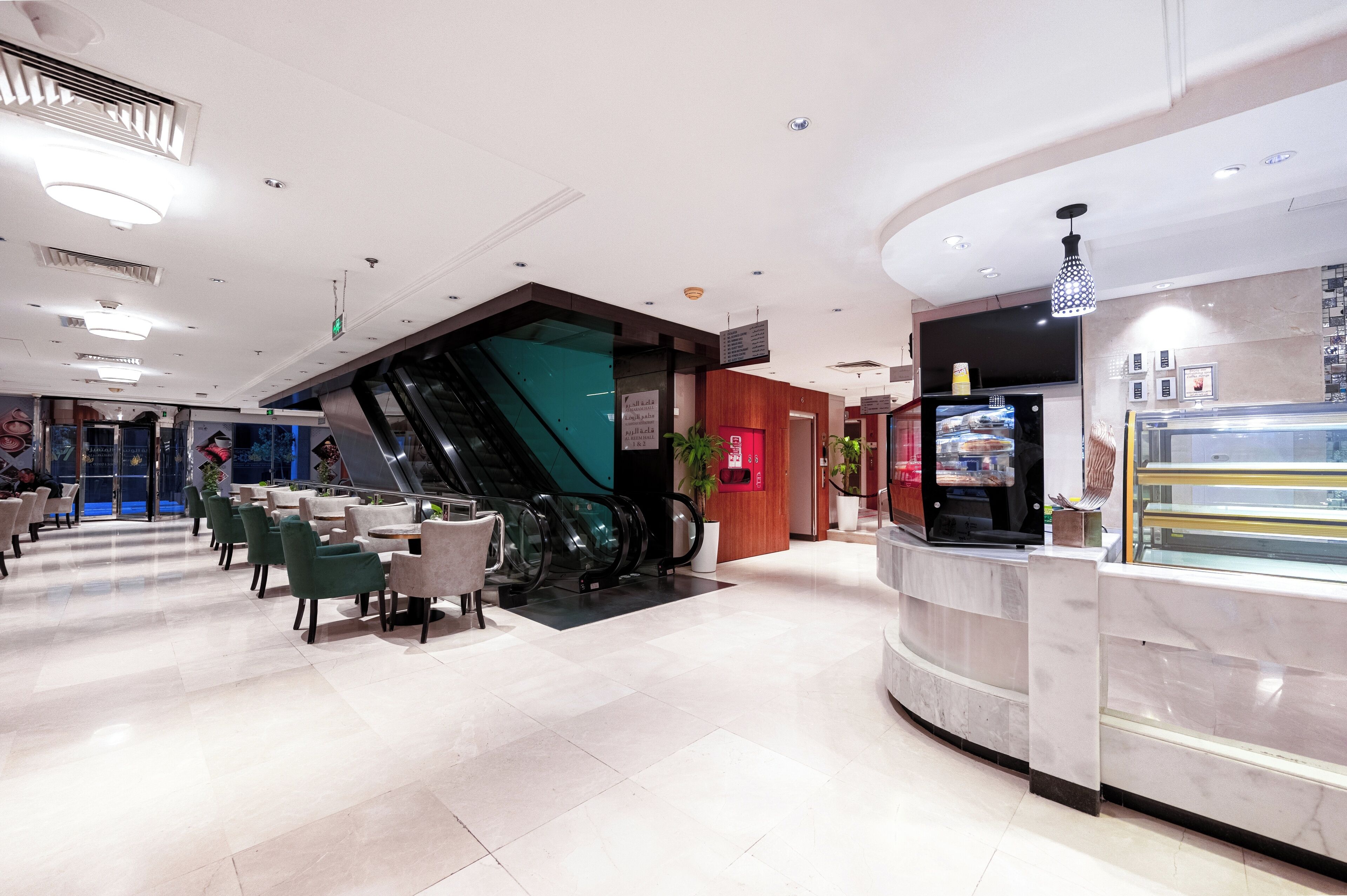 A modern hotel lobby with a marble reception desk, seating area, and an escalator.