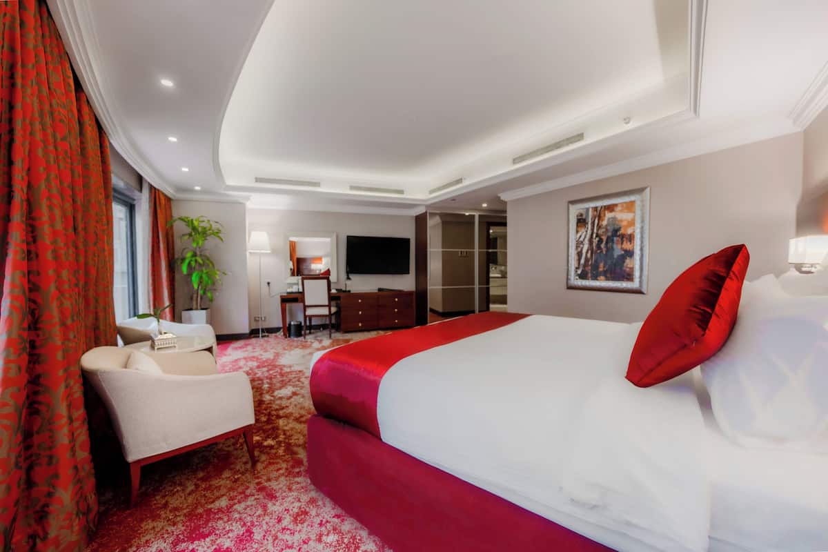 A hotel room with a large bed, a desk, a chair, a TV, and a plant.