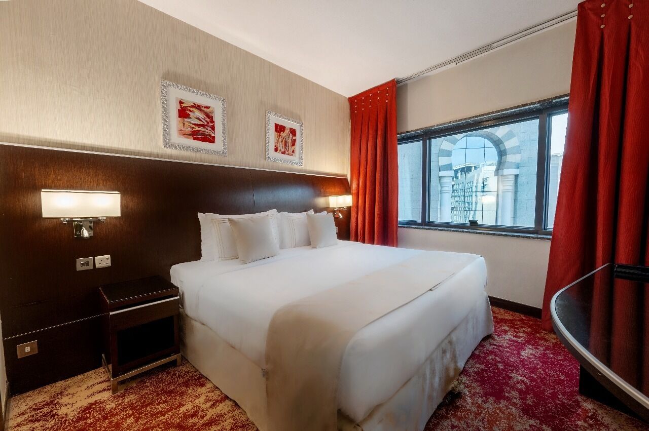 Een hotelkamer met een groot bed, een nachtkastje, een lamp en een raam met gordijnen.