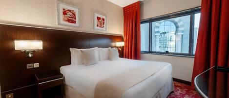 Een hotelkamer met een groot bed, een nachtkastje, een lamp en een raam met gordijnen.