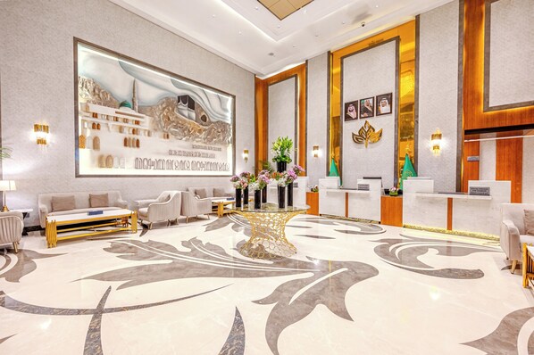 A modern hotel lobby with a reception desk, seating area, and a large wall mural.
