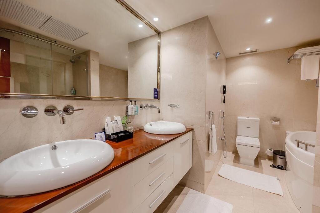 Un baño moderno con dos lavamanos, un espejo grande, una ducha y un inodoro.