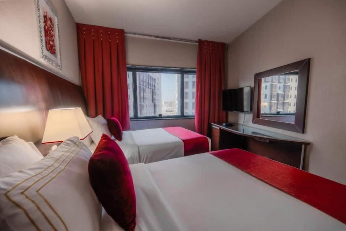 A hotel room with two beds, a TV, a window with a city view, and red curtains.