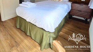 A bedroom with a bed, a wooden headboard, a nightstand, a dresser, a microwave, and a hanging rack. - Deluxe 6 - Single - New Forest (Dibden Purlieu)