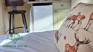 A small kitchenette with a microwave, a coffee maker, and a refrigerator. There is a chair and a bed with a pillow featuring deer illustrations. - Deluxe 6 - Single - New Forest (Dibden Purlieu)