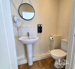 Un baño con un lavabo blanco, un espejo redondo, un inodoro y un rollo de papel higiénico.
