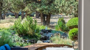 Un jardin agrémenté d’une terrasse en bois, d’une petite cascade et de divers arbustes et arbres.