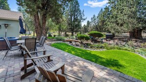 Un espace patio aménagé avec du mobilier d’extérieur, un petit jardin avec un bassin et de grands arbres.