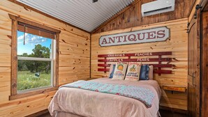 Ein Zimmer mit Holzboden, einem Bett, einem Fenster und einem Wandschild mit der Aufschrift 'ANTIQUE'.