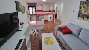 Un espace de vie compact comprenant un téléviseur, un canapé, une table à manger, une cuisine et un ventilateur de plafond.