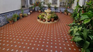 Une cour avec un sol carrelé, des plantes en pot et une fontaine centrale.