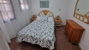 Une chambre à coucher comprenant un lit, des tables de chevet, une commode, un ventilateur de plafond et une fenêtre avec des rideaux.