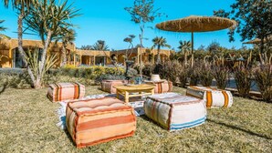 Un patio con mobiliario exterior, palmeras y un paraguas de paja.