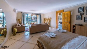 Una habitación de hotel moderna con una cama grande, dos sofás, una zona de comedor con mesa y vistas al exterior.