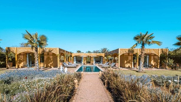 Un resort con piscina central, palmeras y un cielo azul despejado.