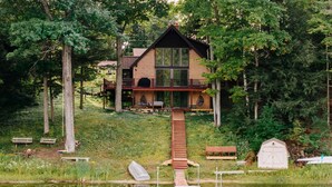 Un chalet au bord du lac, doté d’une terrasse en bois, d’un petit quai pour bateaux et d’une grande fenêtre donnant sur l’eau.