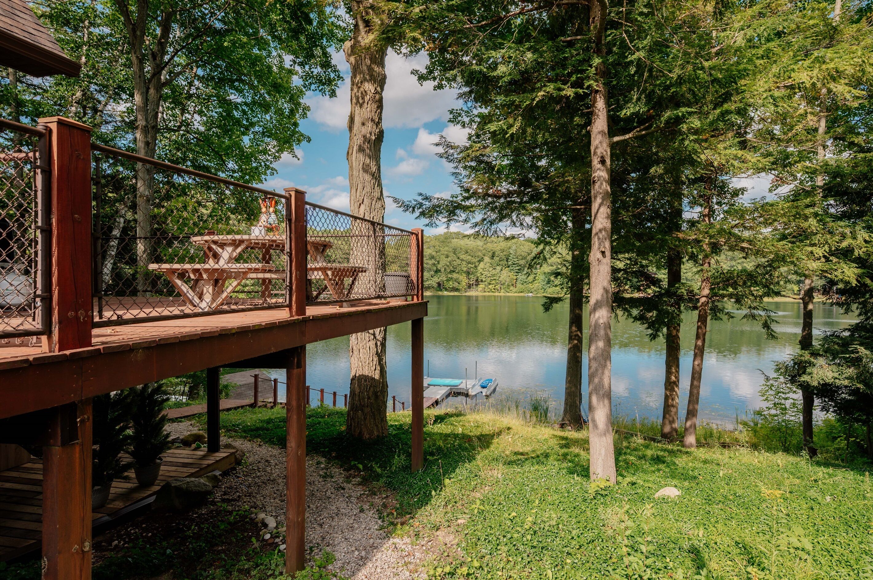 Une terrasse en bois avec une table de pique-nique, d’où l’on a vue sur un lac, le tout entouré d’arbres.