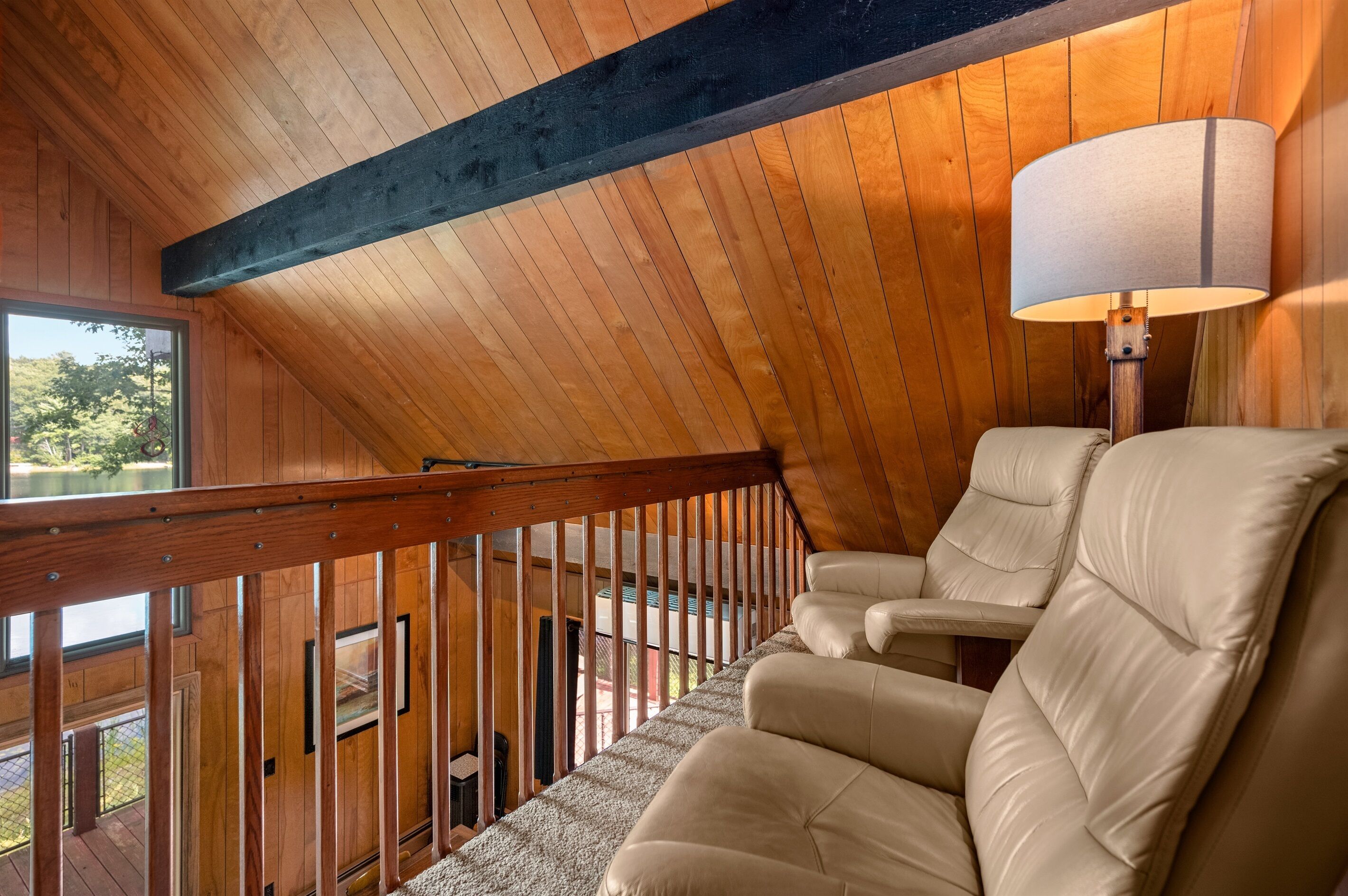 A wooden interior with a staircase, leather chairs, and a lamp.