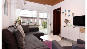 A modern living room with a grey sofa, a white coffee table, and a flat-screen TV on a wooden cabinet. - Reihenhaus Land and Sea in Busum (Westerdeichstrich)