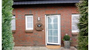 A brick building with a white door and windows, a small porch area, and a potted plant. - Reihenhaus Land and Sea in Busum (Westerdeichstrich)