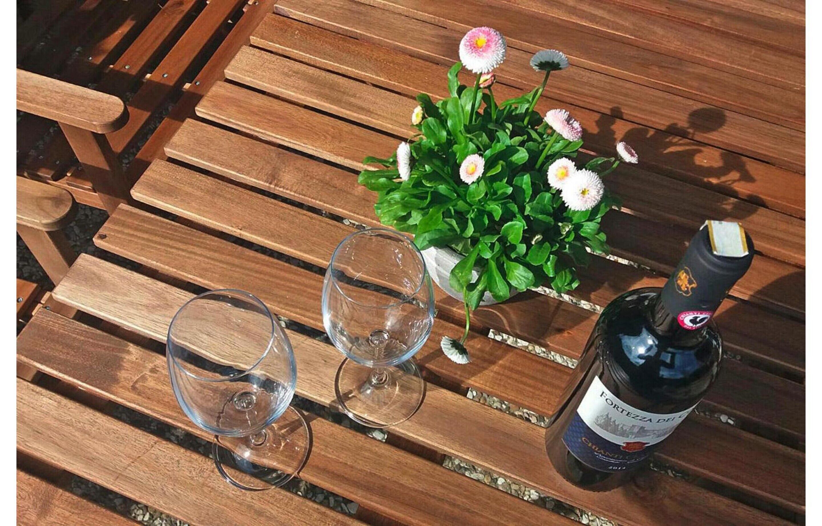 A wooden table with two empty wine glasses, a bottle of wine, and a potted plant with flowers.