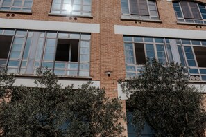 Ein mehrgeschossiges Gebäude mit Backsteinfassade und großen Fenstern, wobei sich ein offenes Fenster im zweiten Stock befindet.