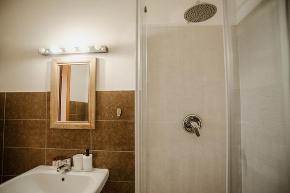 Un baño con lavamanos, espejo, artículos de aseo y cabina de ducha.