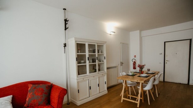 Un salon avec un canapé rouge, un meuble blanc, une table à manger en bois avec des chaises et une porte blanche.