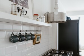 Een keuken met een witte betegelde spatwand, een gasfornuis en een hangende pannendroger.