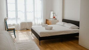 Une chambre à coucher comprenant un lit, une chaise, une table de chevet et une fenêtre avec des rideaux légers.