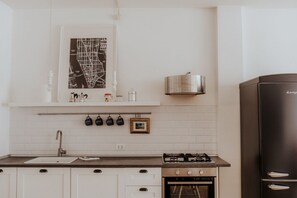 Una cocina con armarios blancos, una campana extractora de acero inoxidable, un refrigerador negro y un mapa colgado en la pared.
