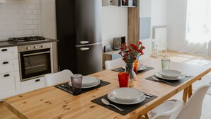 Une cuisine moderne avec un réfrigérateur noir, des armoires blanches et une table à manger en bois, mise avec des assiettes, des verres et un vase rempli de fleurs rouges.