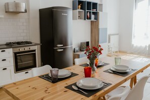 Een moderne keuken met een zwarte koelkast, witte kasten en een houten eettafel gedekt met borden, glazen en een vaas rode bloemen.