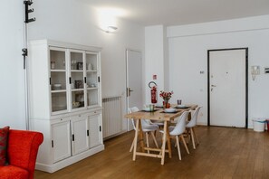 A dining area with a wooden table and white chairs, a white cabinet with glass doors, and a red fire extinguisher on the wall.
