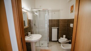 Een badkamer met een glazen douchecabine, een wastafel op voet, een toilet en een bidet.