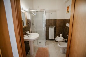 Ein Badezimmer mit Duschkabine aus Glas, einem Standwaschbecken, einer Toilette und einem Bidet.