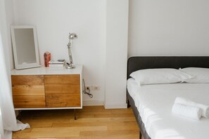 Un dormitorio con una cama, una mesita de noche con lámpara, un espejo y un aparador de madera.