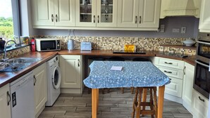 Een keuken met witte kastjes, een magnetron, een wasmachine en een eettafel met een blauwe tafelkleed.