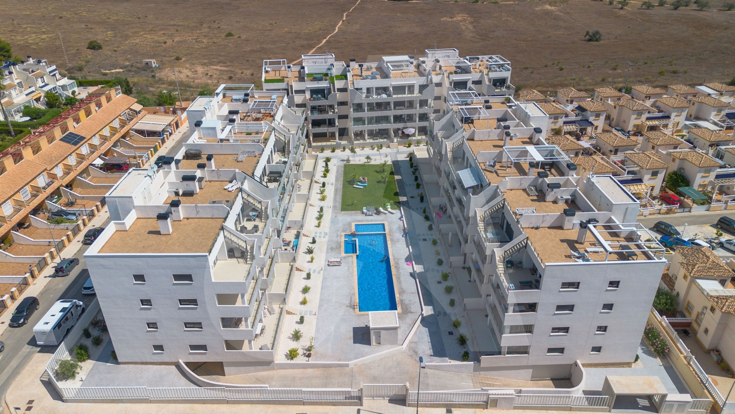 A modern residential complex with multiple apartment buildings, a central swimming pool, and a well-maintained lawn.