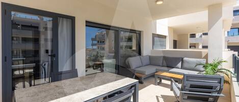 A modern outdoor living area with a dining table, sofa, and a grill station.