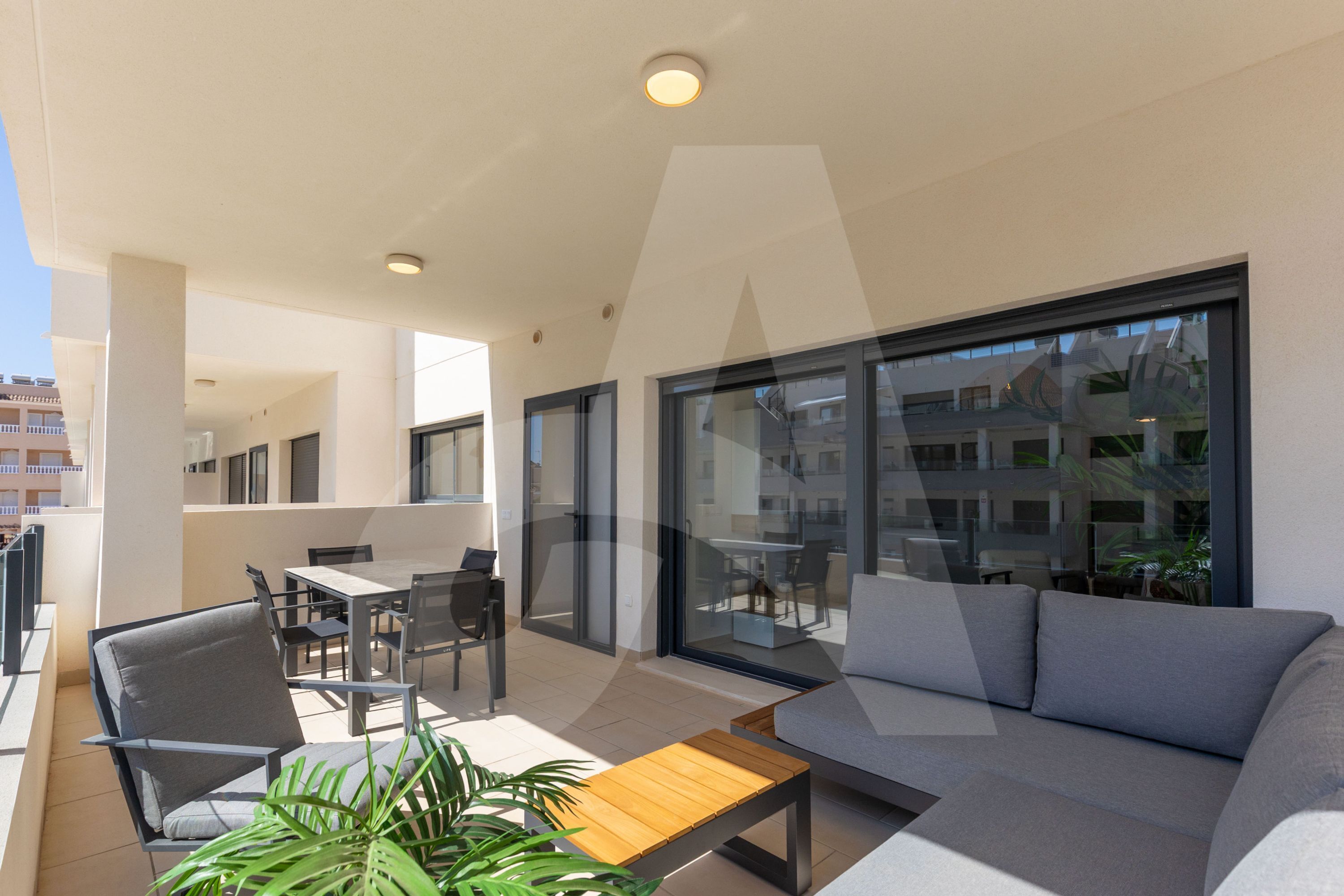Un espace de vie extérieur moderne comprenant un canapé, des fauteuils, une table et un mur de verre offrant une vue sur la ville.