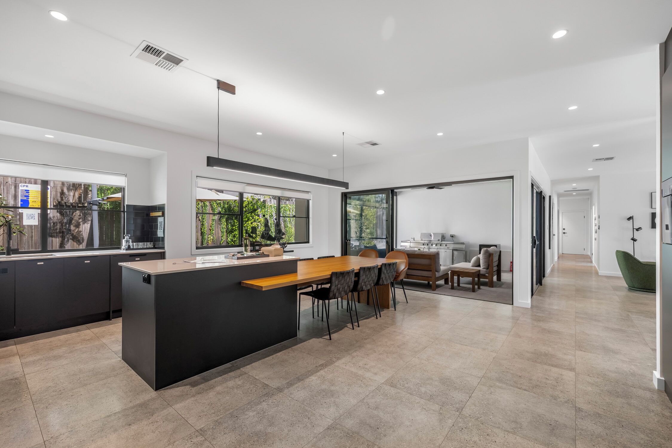 A modern kitchen with a central island, dark cabinetry, and a dining area with chairs and a table.