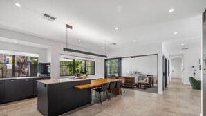 Une cuisine moderne dotée d’un îlot central, de meubles de rangement aux couleurs sombres et d’un coin repas avec des chaises et une table.