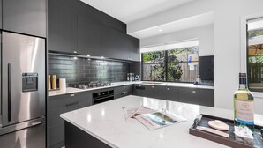 Une cuisine moderne avec des meubles de couleur sombre, un réfrigérateur en acier inoxydable et un plan de travail en marbre.