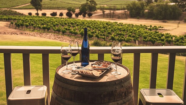 Une table avec des verres à vin, une bouteille et des amuse-gueules, posée sur une barrique, d’où l’on a vue sur un vignoble.