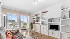 Un salon moderne avec un canapé, une table basse, un téléviseur et des étagères blanches où sont disposés des livres et des objets décoratifs.