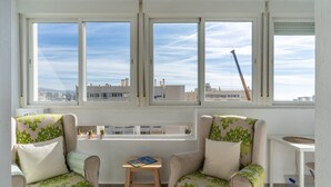 Une pièce comprenant deux fauteuils, une petite table et offrant une vue sur la ville grâce à de grandes fenêtres.