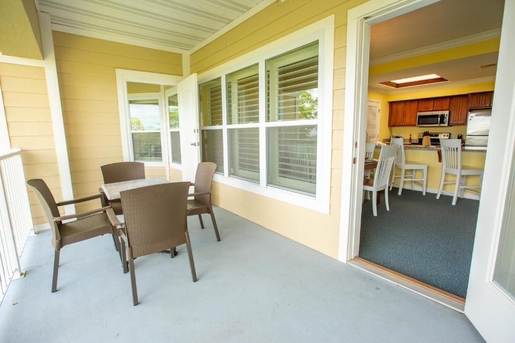 Un patio techado con una mesa y sillas, una zona de cocina con armarios y electrodomésticos, y una puerta que da al interior.