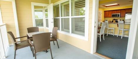 Un patio techado con una mesa y sillas, una zona de cocina con armarios y electrodomésticos, y una puerta que da al interior.